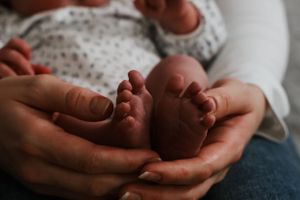 Close-up of two adult hands gently cupping the small bare feet of a newborn.
