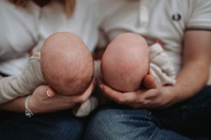 Two parents holding twin newborn babies side by side, showing the tops of their heads.