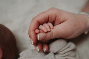 Adult hand gently holding a newborn baby's tiny fist, showcasing the size difference between parent and child.