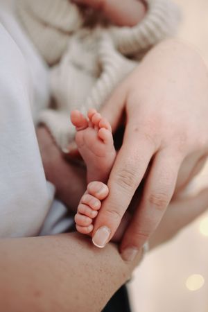 Parent's hand tenderly cradling a newborn baby's tiny bare feet against a soft white background.