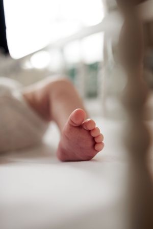 Close-up of a newborn baby's tiny bare foot resting on a white surface in soft light.