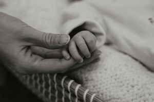 Black and white image of adult hand holding tiny newborn baby fingers.