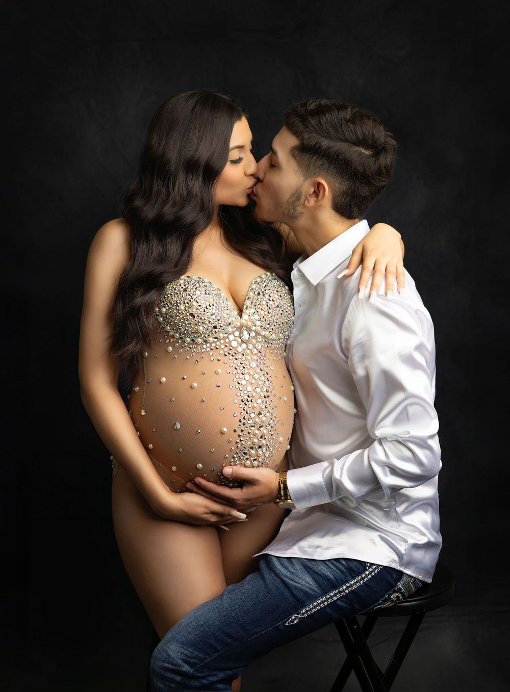 Intimate maternity portrait with sparkly dress against dark backdrop.