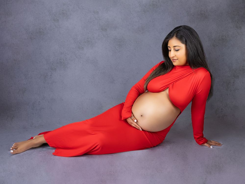 Artistic maternity portraits featuring a woman in red dress posing gracefully against a dark grey background.