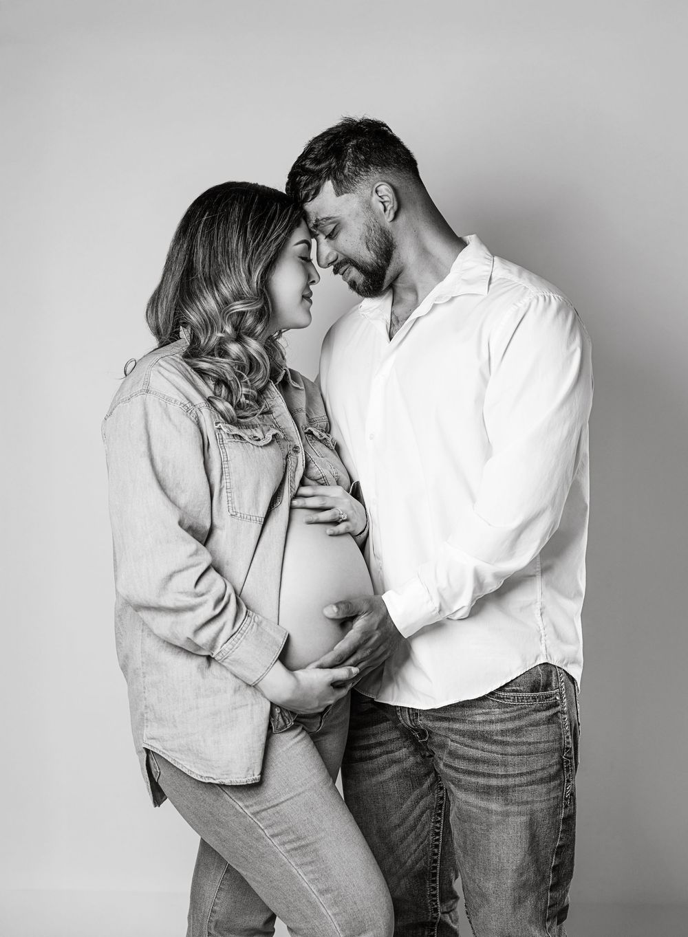 A pregnant woman and her husband embrace affectionately in a black and white portrait.