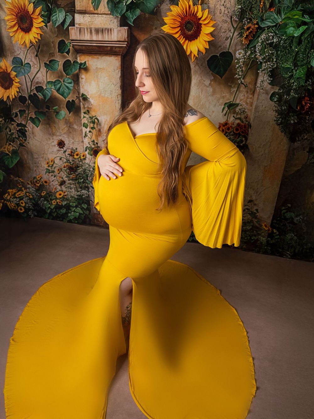 A woman in a bright yellow dress poses gracefully against a rustic wall adorned with vibrant sunflowers.