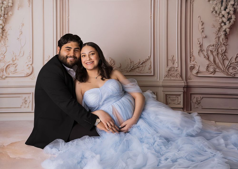 A romantic couple poses in an elegant room with ornate walls and a flowing light blue tulle gown.