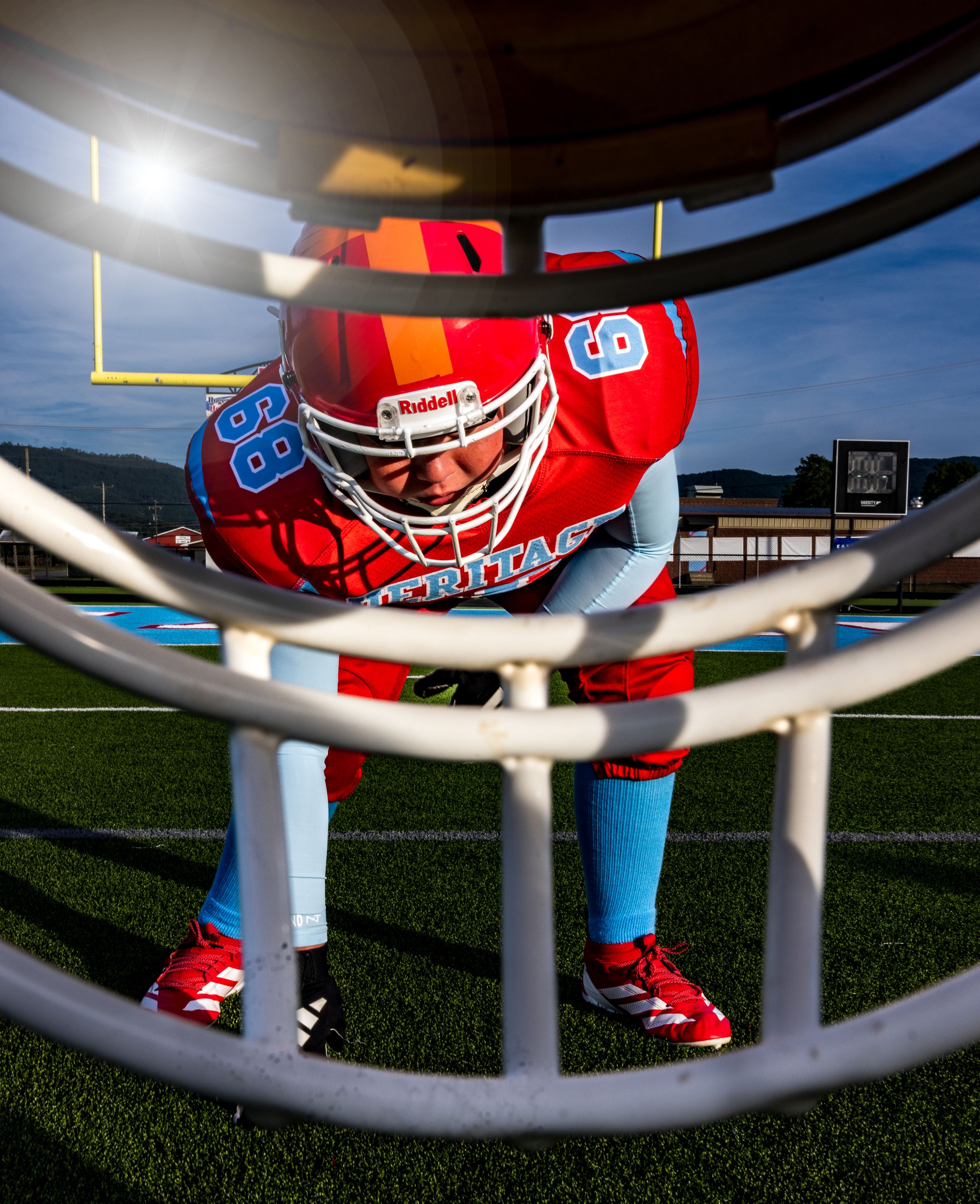 Low-angle view through football helmet facemask showing red and blue uniform on artificial turf field.