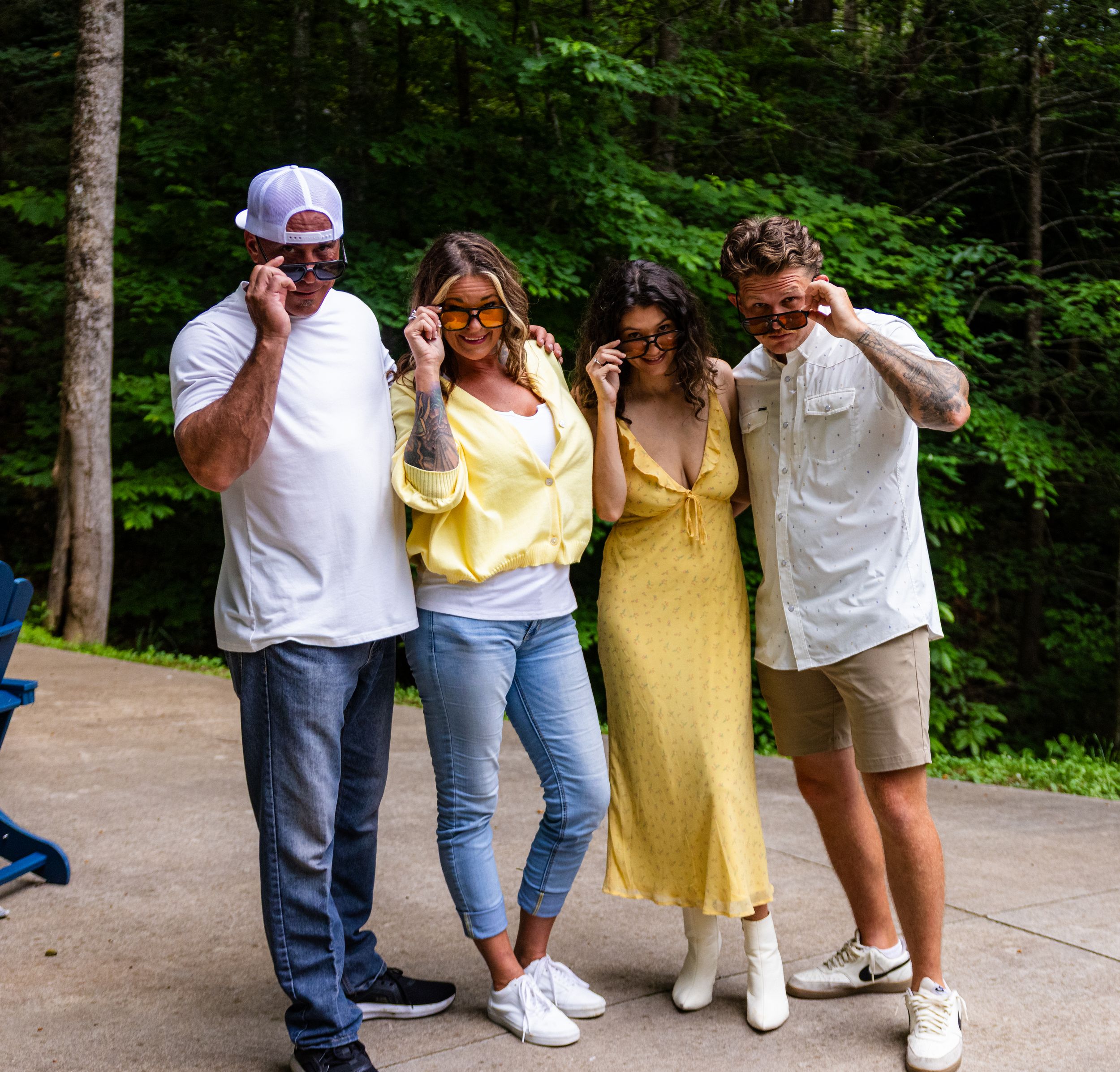 Four friends laughing and posing together outdoors with lush green forest trees in the background.