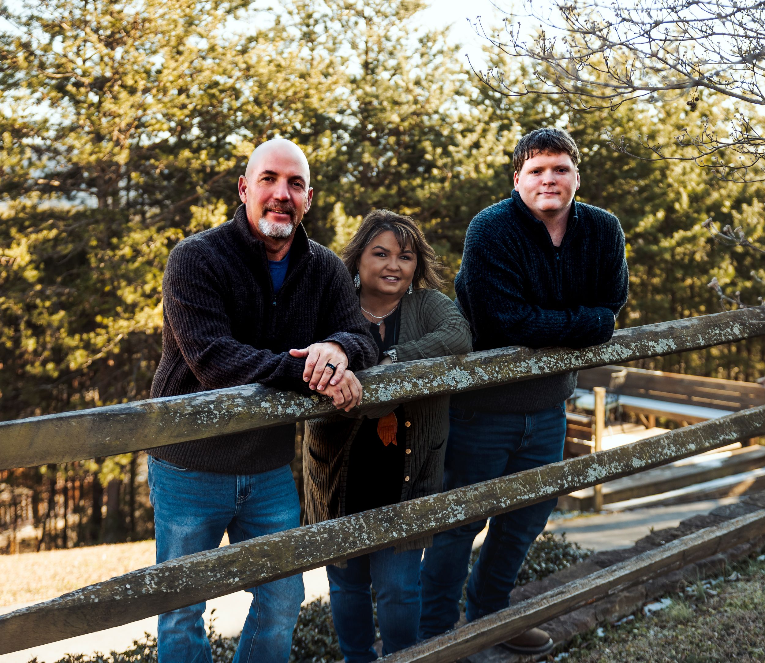 Group of people leaning on a rustic wooden fence in an outdoor setting during golden hour lighting.