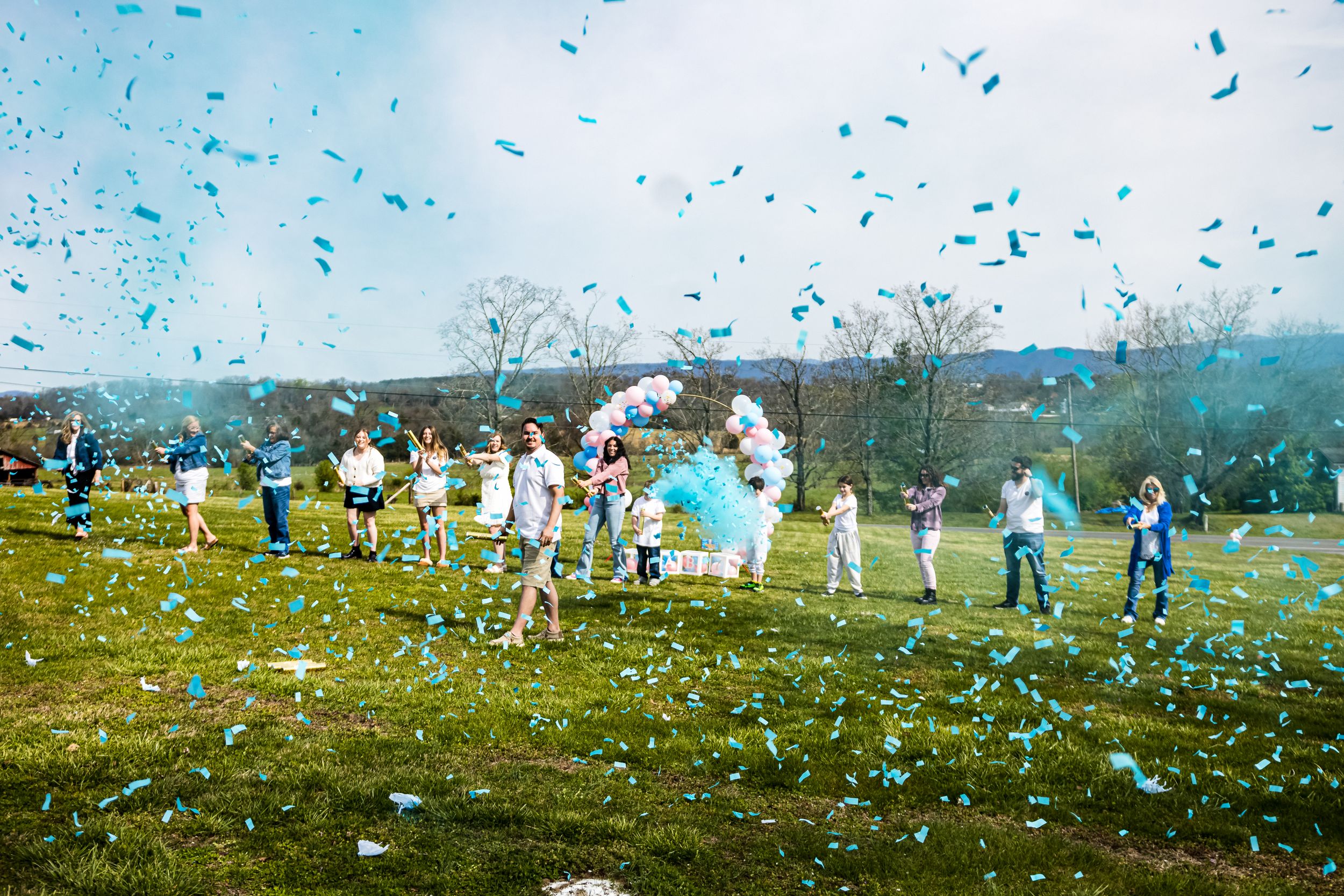 Large group celebrating with blue confetti and smoke bombs in an open field.