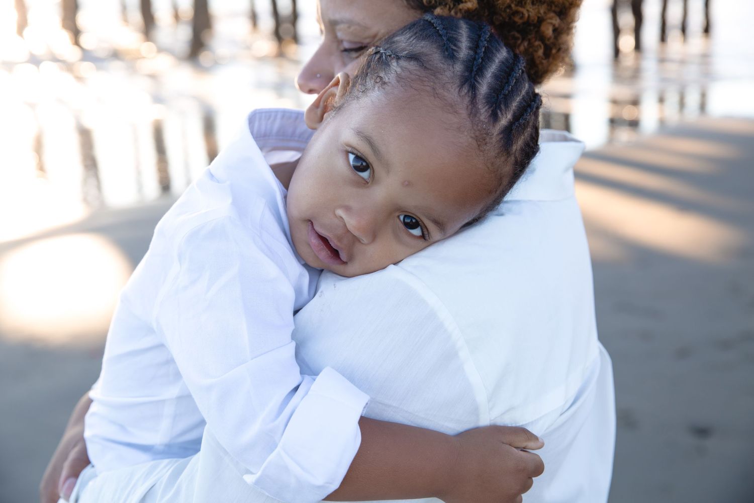 A young person wearing a white shirt smiles while giving a warm embrace outdoors in natural lighting.