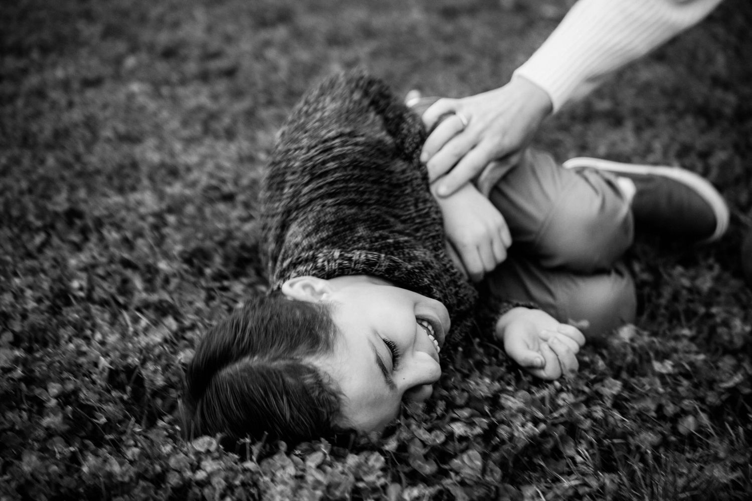 A person in a sweater lies on grass in dramatic black and white photography.