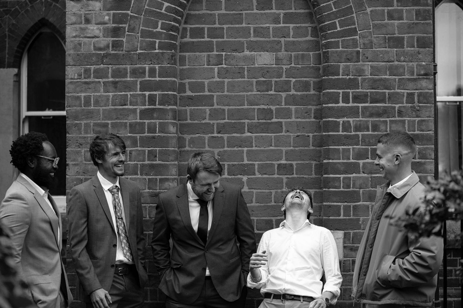 A group of people in formal attire gather outside a brick building in what appears to be a historical black and white photo.