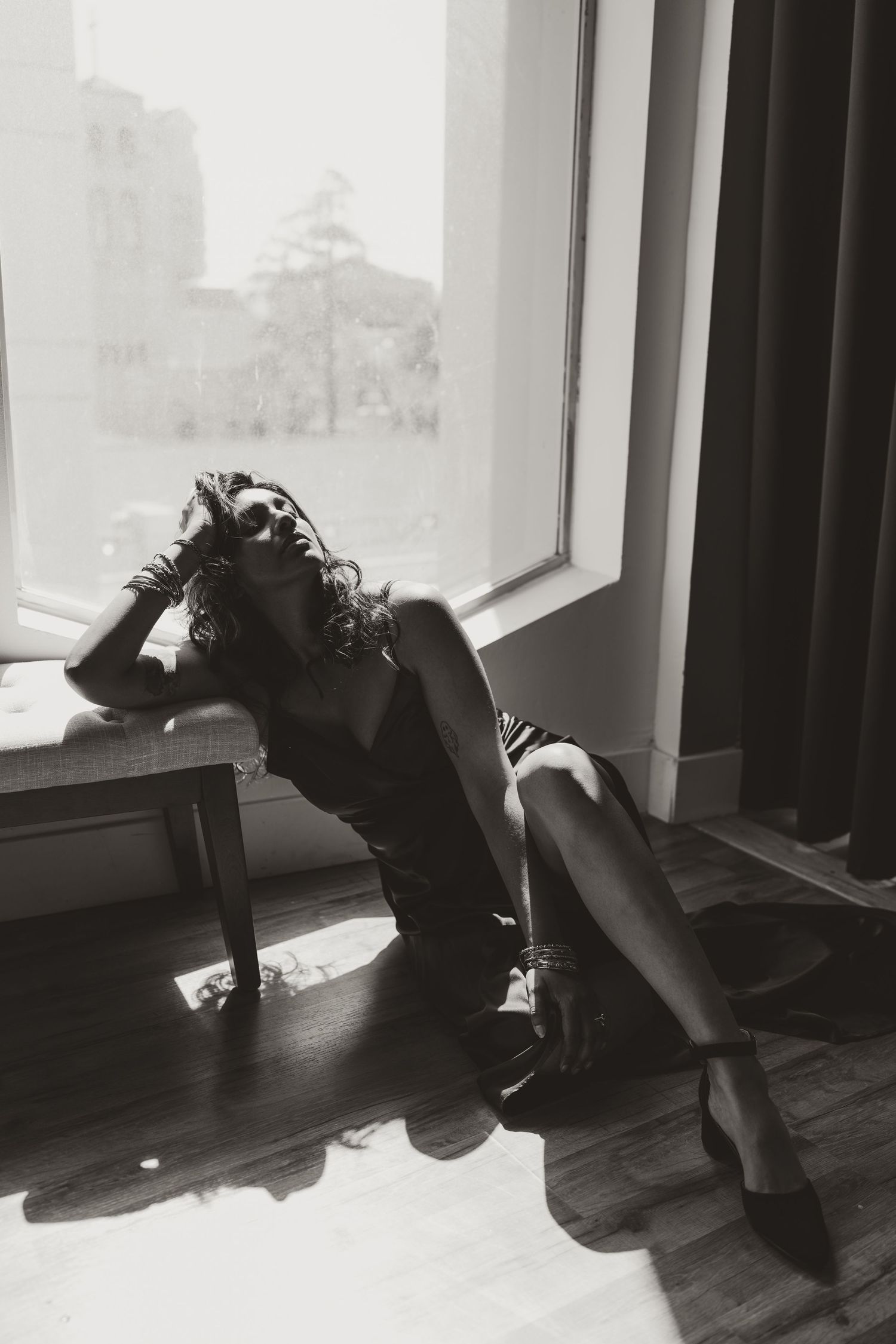 A black and white artistic photograph of a figure reclining on furniture near a window in silhouette.