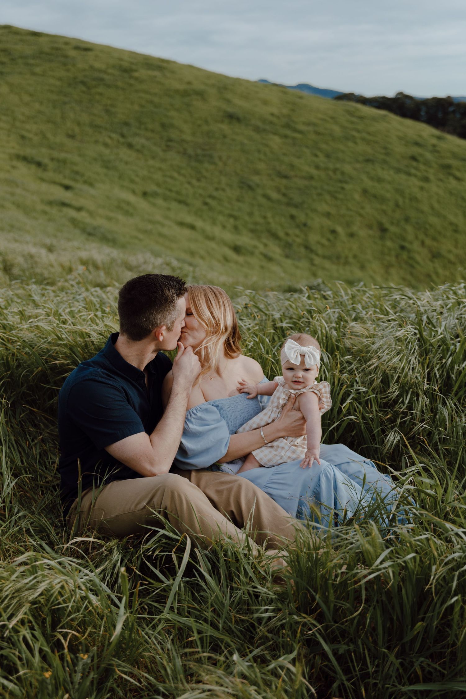 A family shares an intimate moment together while sitting in tall grass on a hillside.