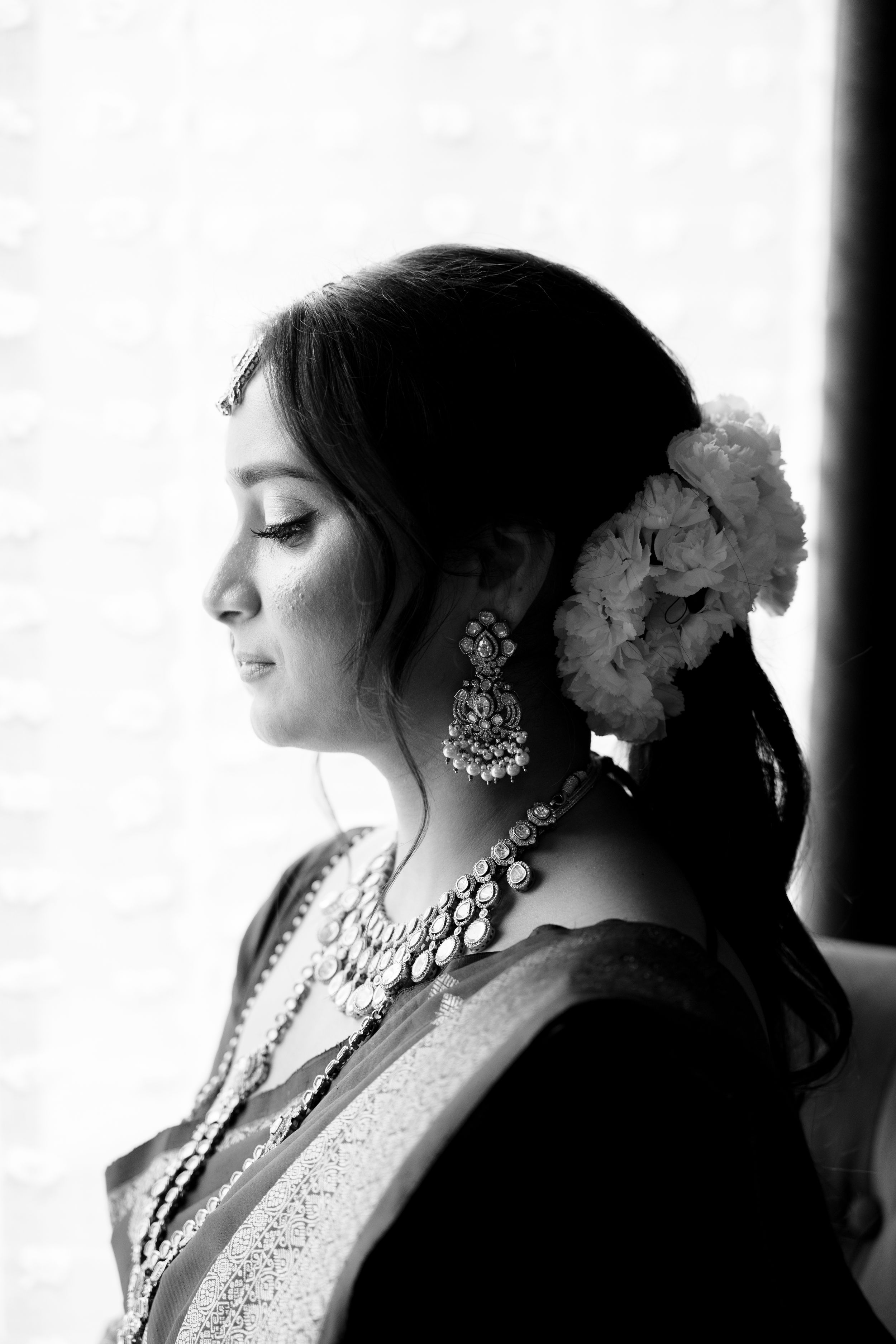 A black and white portrait showcasing elegant jewelry and floral hair accessories.