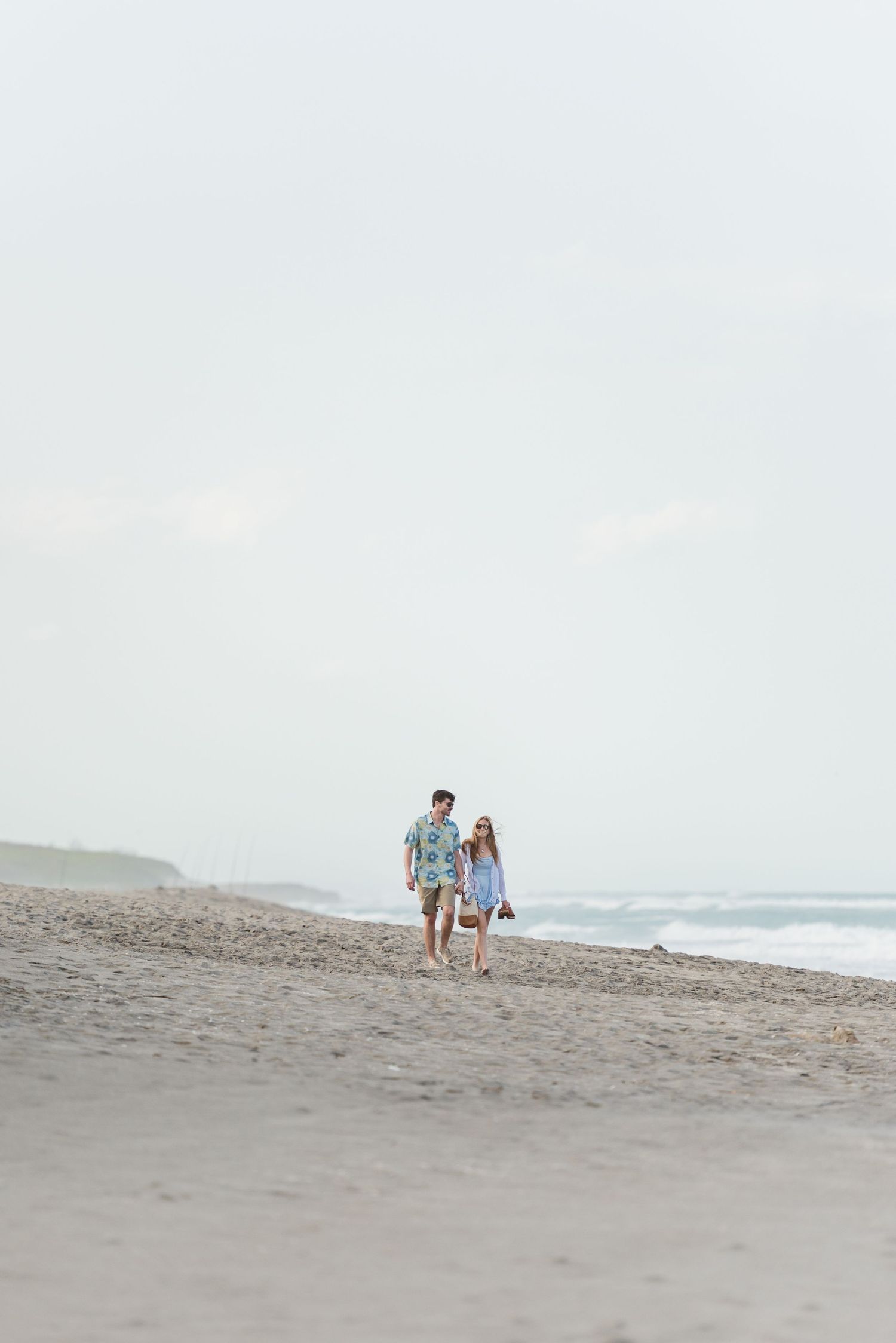 A couple strolls along a misty beach shoreline.
