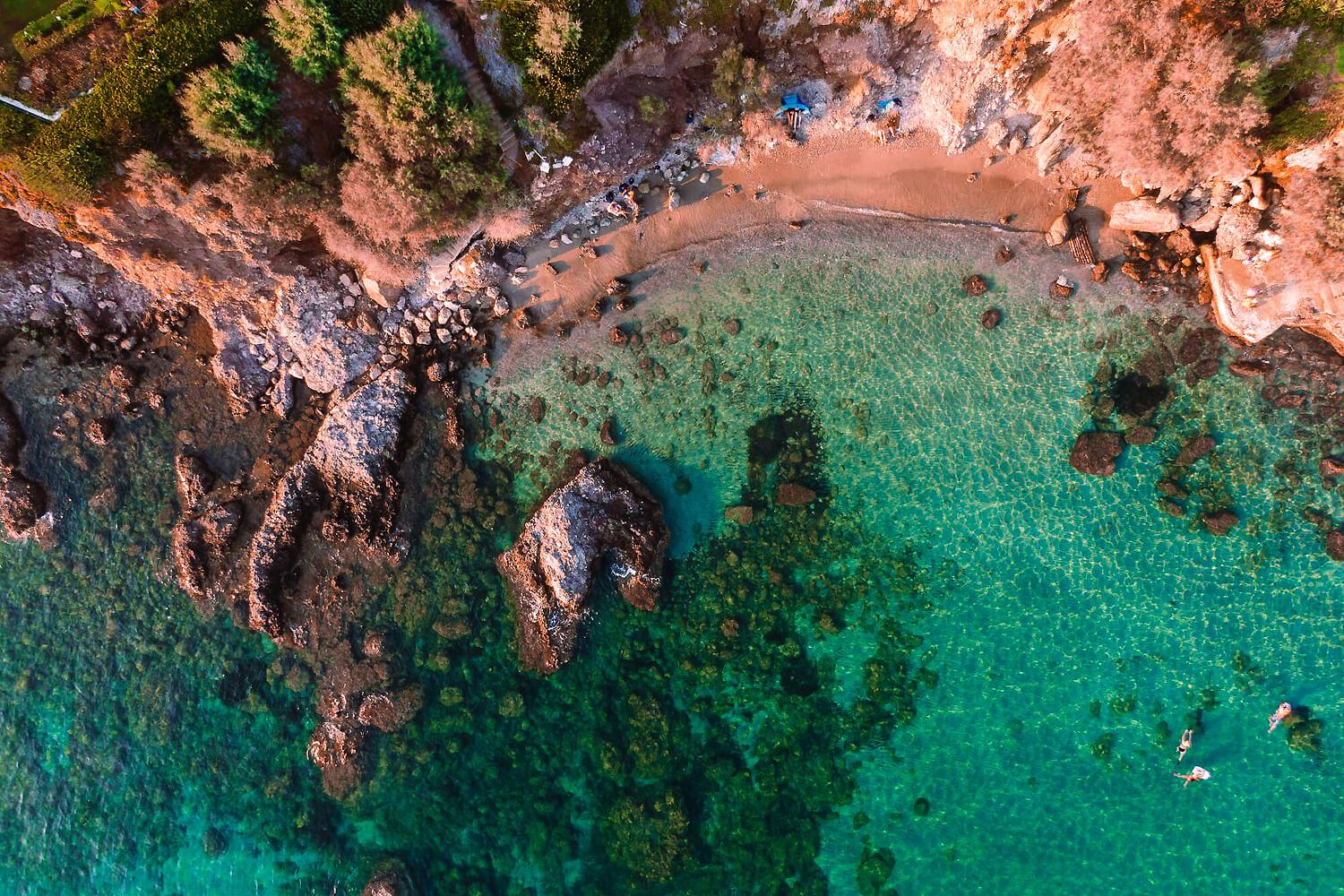 Aerial view of a rocky Mediterranean cove with crystal-clear turquoise waters and scenic coastline.