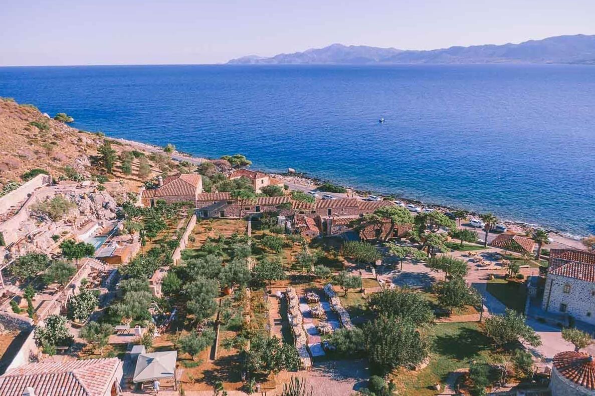 Aerial view of a Mediterranean coastal village with lush gardens, historic ruins, and blue sea waters.
