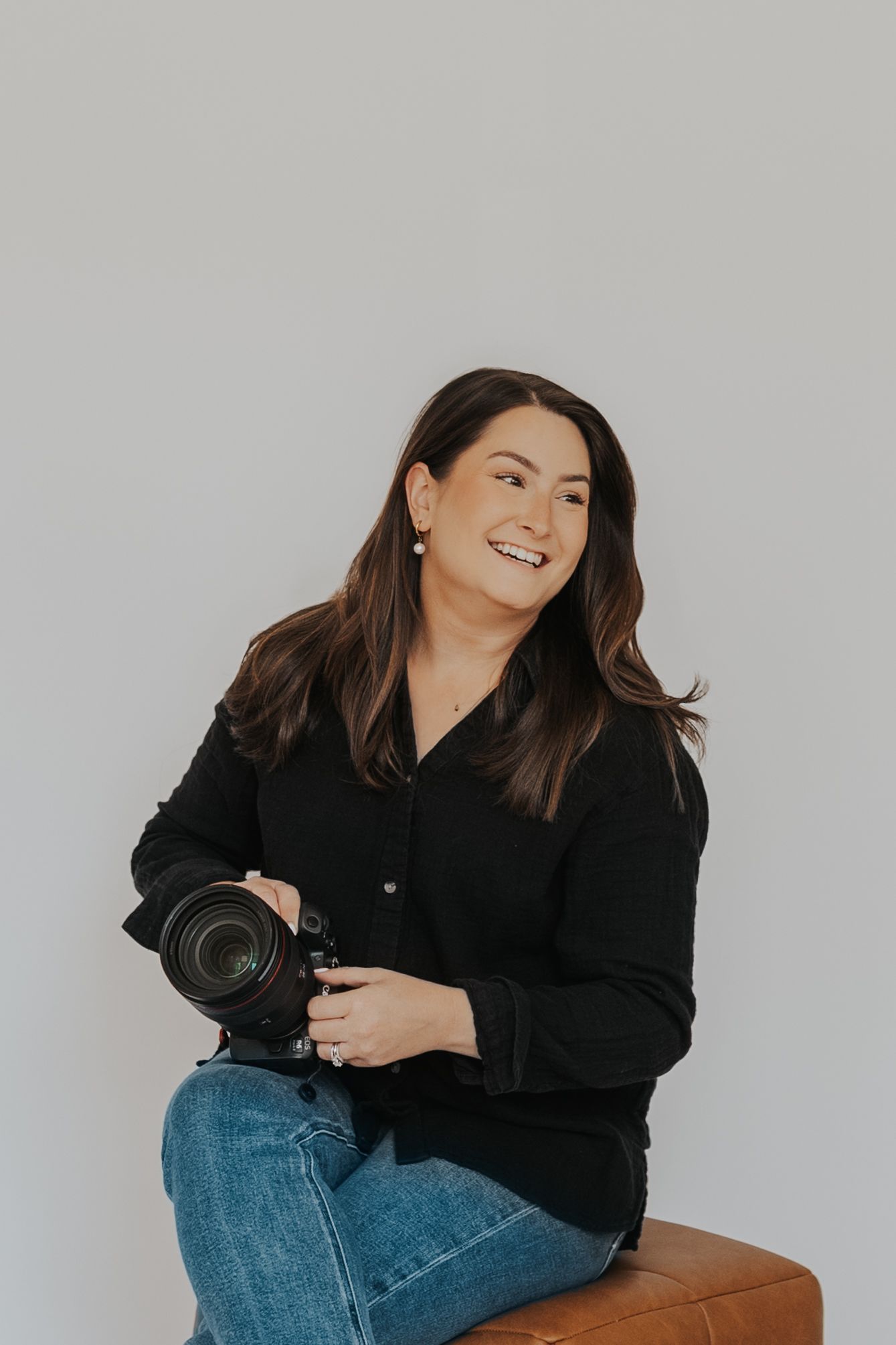 Candid portrait of photographer laughing while holding camera against white backdrop.