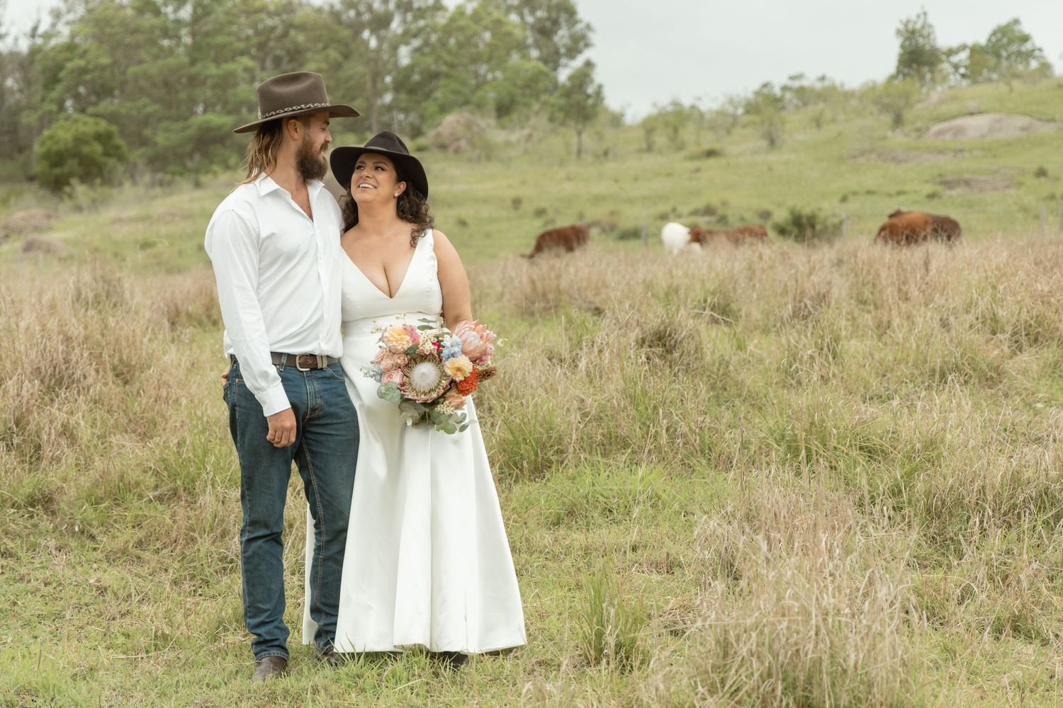 Rural landscape with grazing cattle and figures in wedding attire.