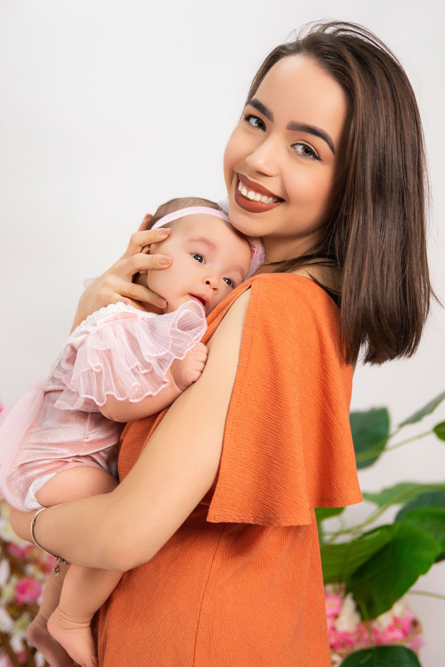 Mother in orange dress holding baby in pink outfit during studio photoshoot.