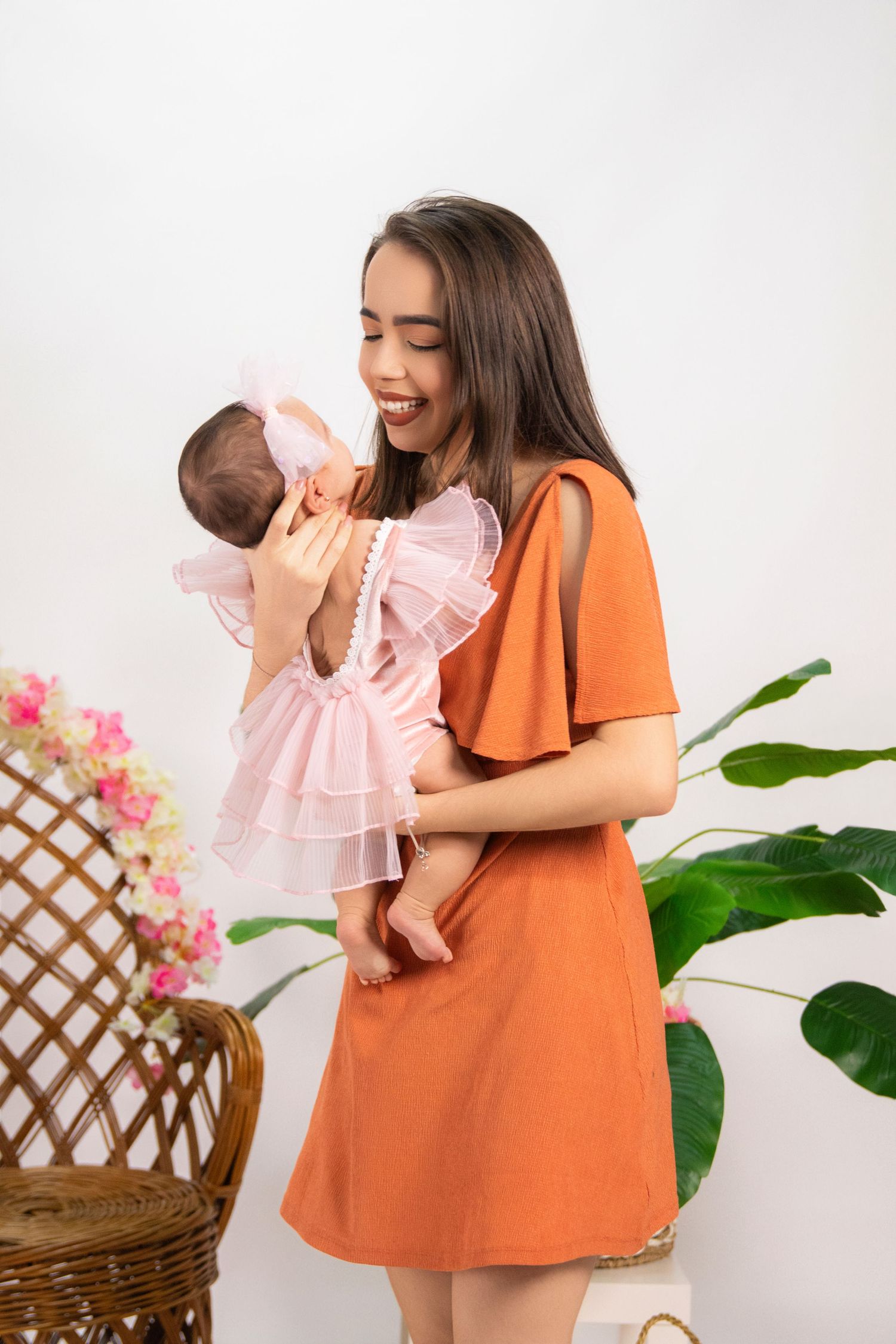 Mother and baby in coordinating orange and pink outfits posing with indoor plants.