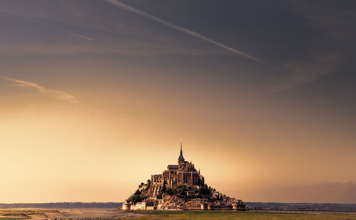 Mont Saint-Michel castle rises from the sea during golden sunset in Normandy, France.