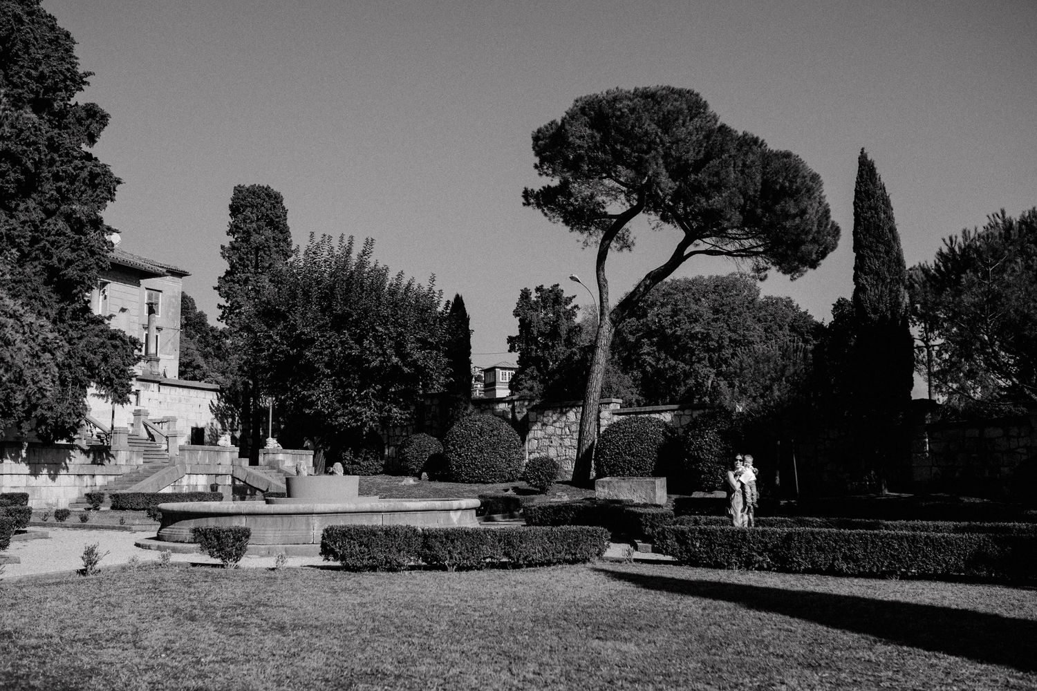 Black and white photo of a Mediterranean garden with stone paths and cypress trees.