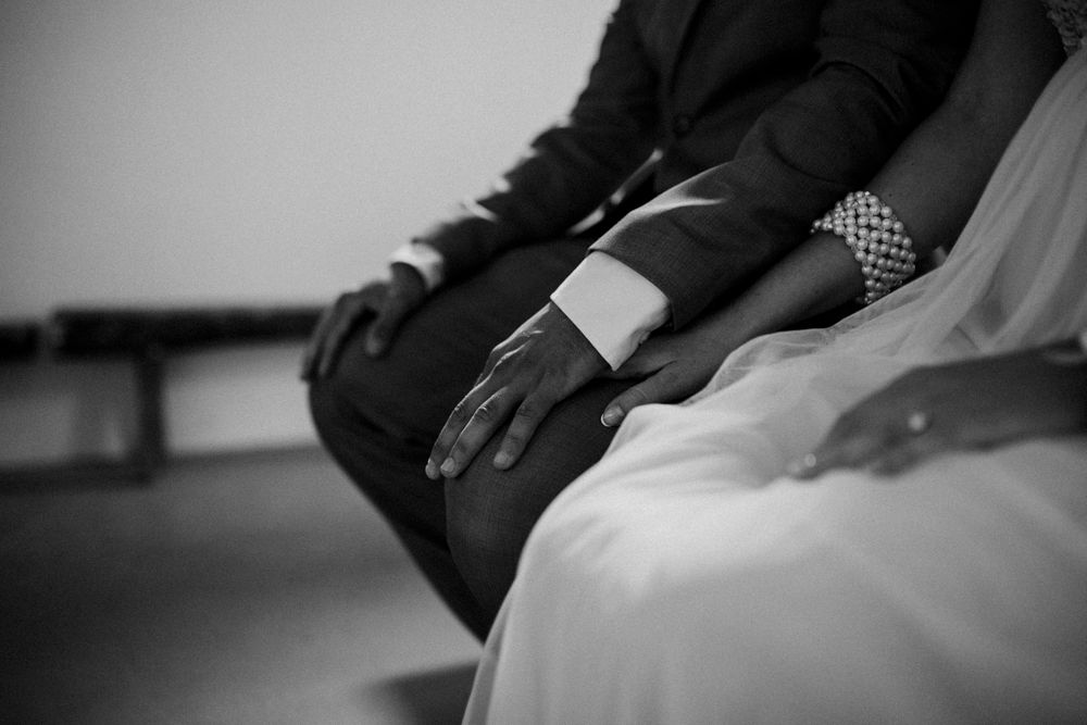 Black and white closeup of hands resting on formal attire during wedding ceremony.