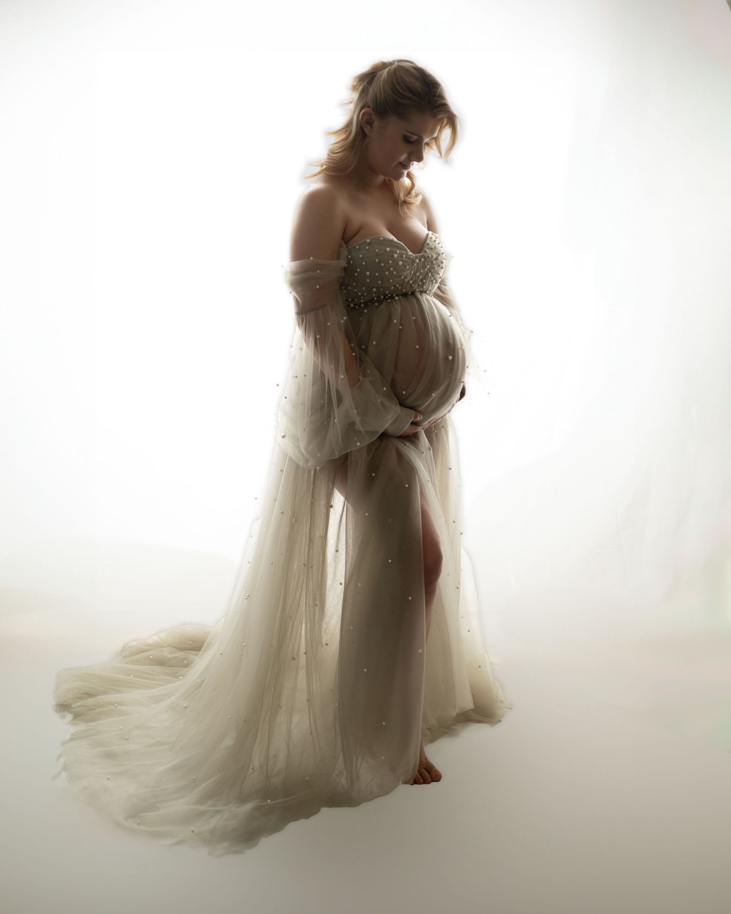 Artistic maternity portrait in flowing white gown against light backdrop.