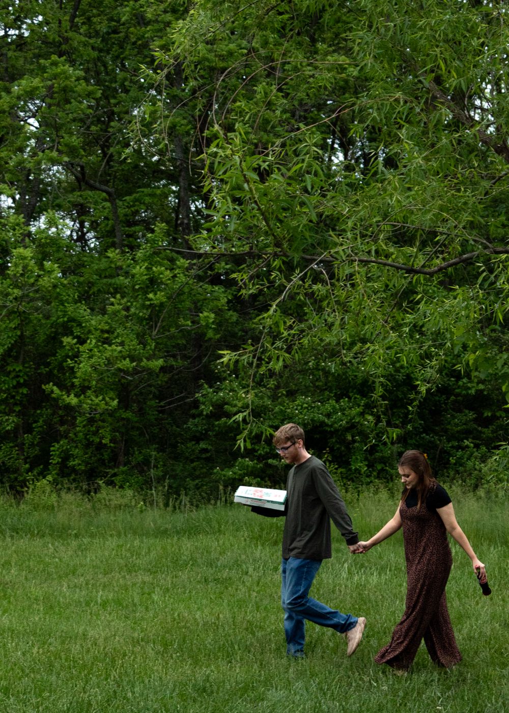 Two people playfully running through a lush green field on a sunny day.