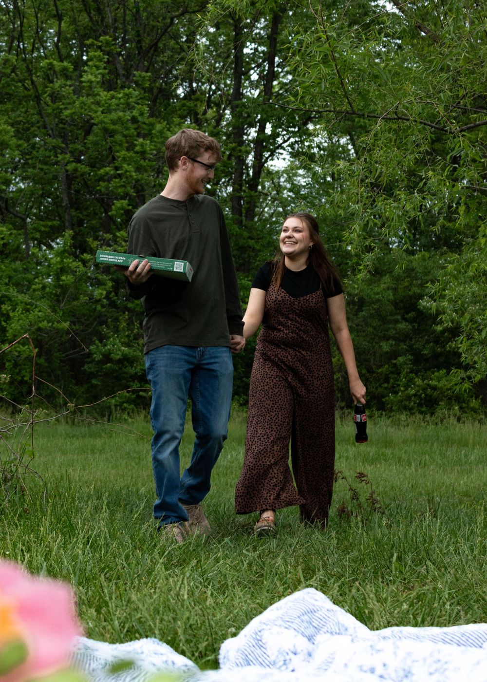Couple dancing and laughing in a grassy meadow with white blanket.