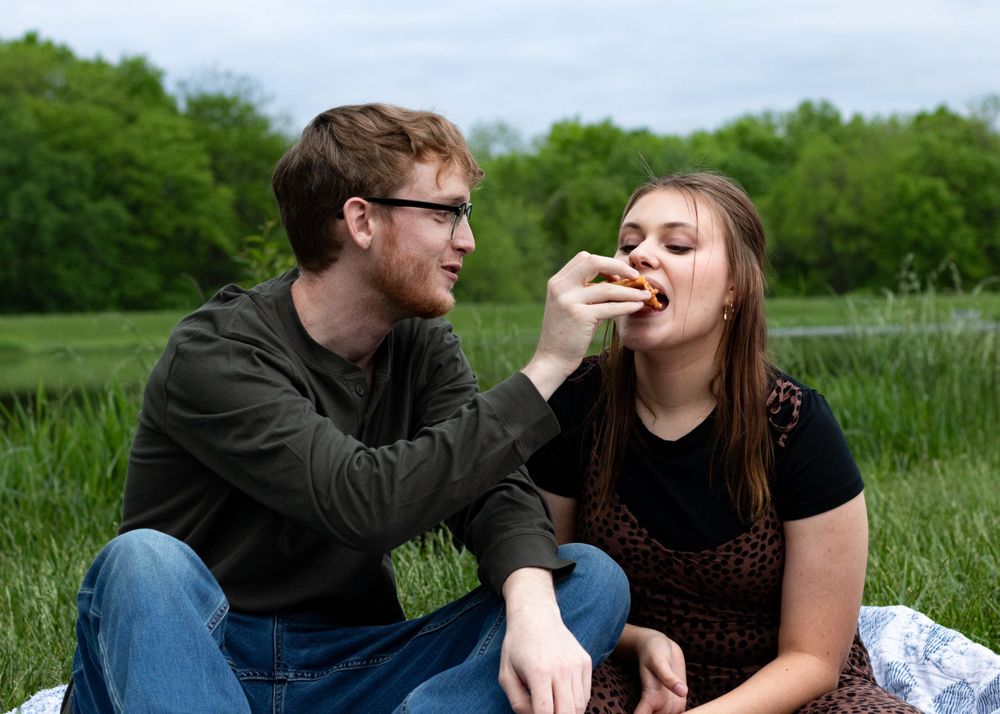 Couple sharing playful moments on picnic blanket in green field.