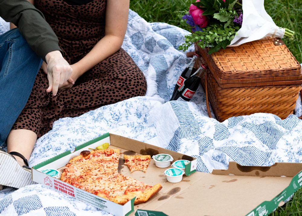 A couple enjoying a romantic picnic with food spread out on a blanket by a lake.