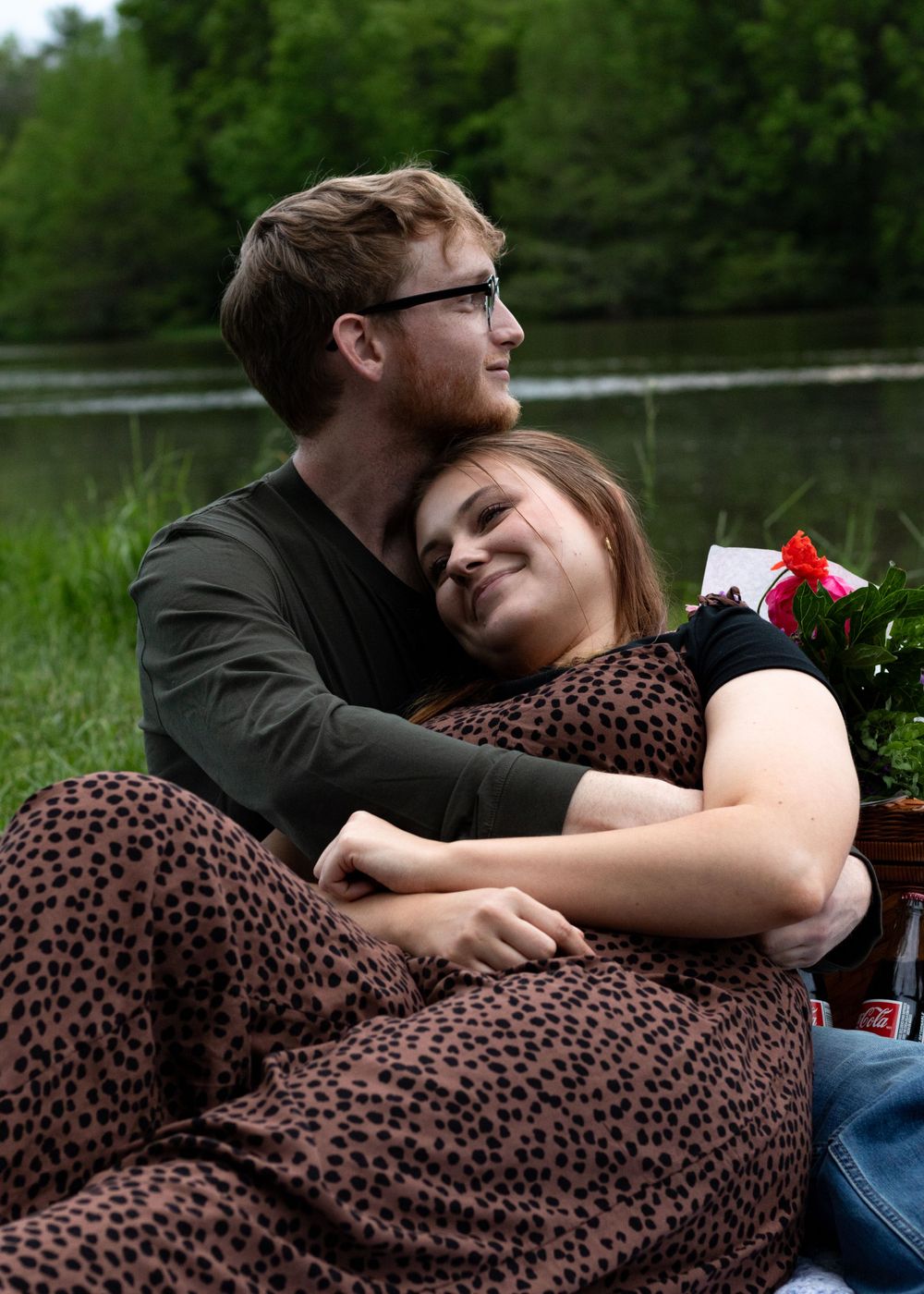 Two people cuddling together on a picnic blanket in a park setting.