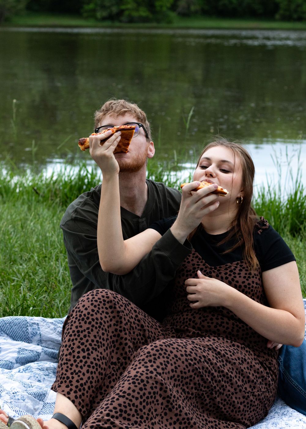 Couple sharing pizza while relaxing on a blanket during an outdoor picnic.