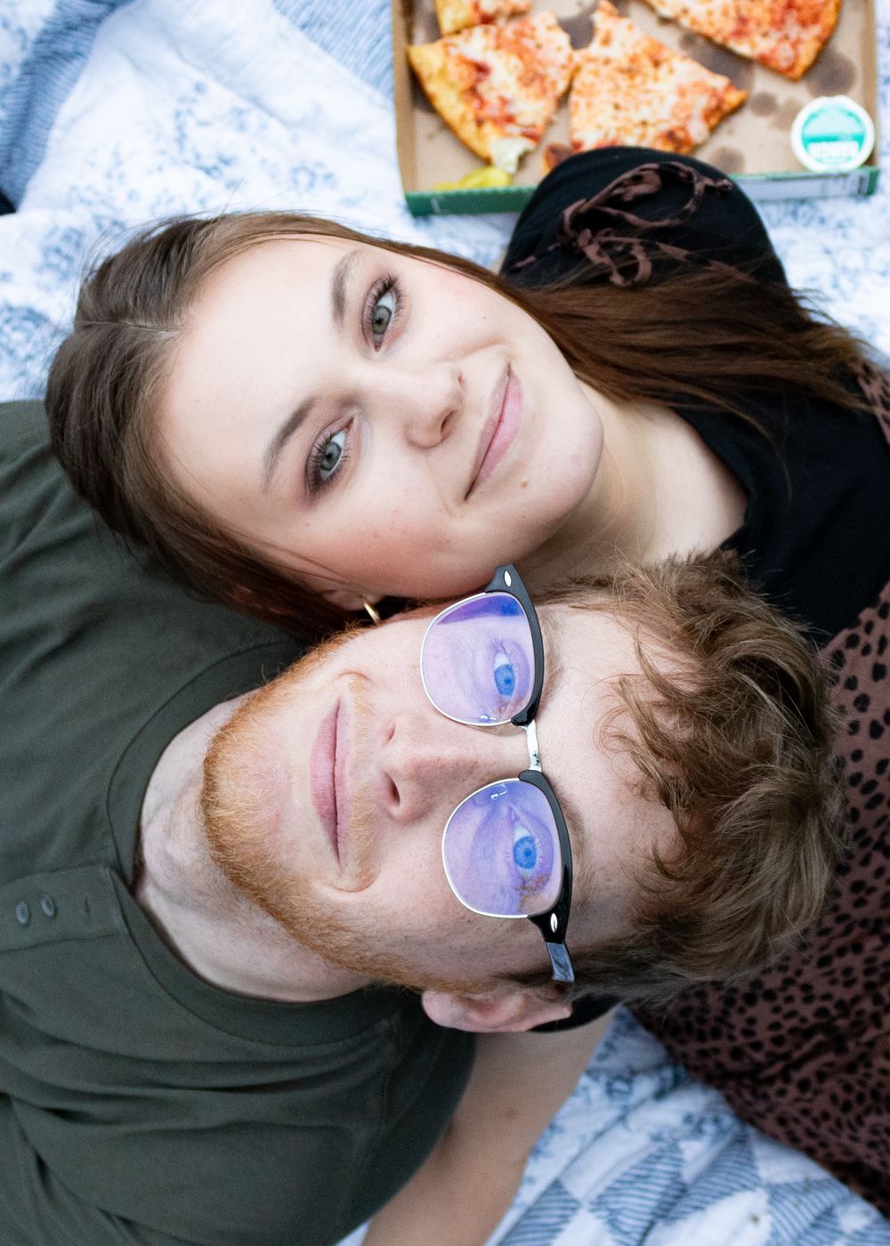 A couple lying on a blanket taking selfies together outdoors.