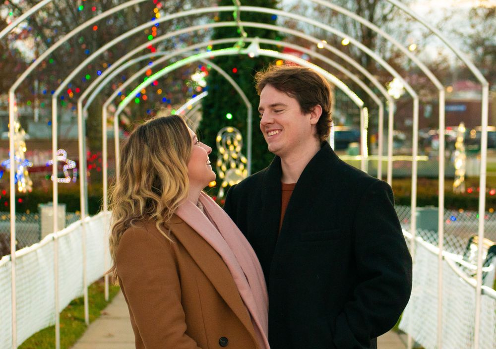 A couple shares a happy moment under an archway decorated with Christmas lights.