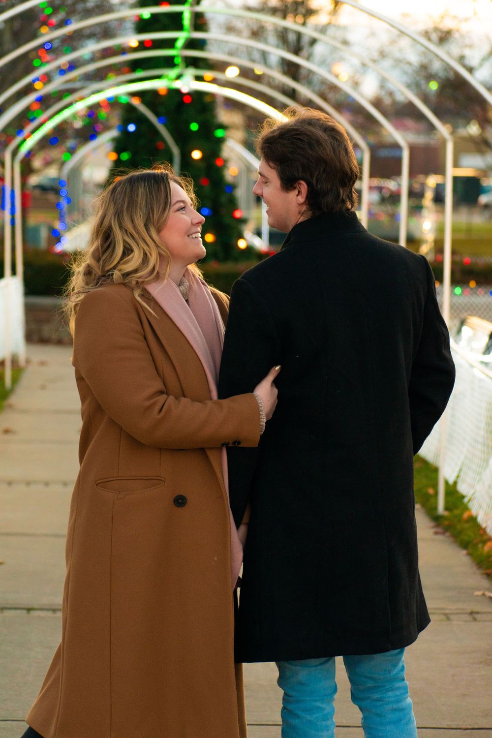 A couple laughing together while walking under an illuminated holiday archway.