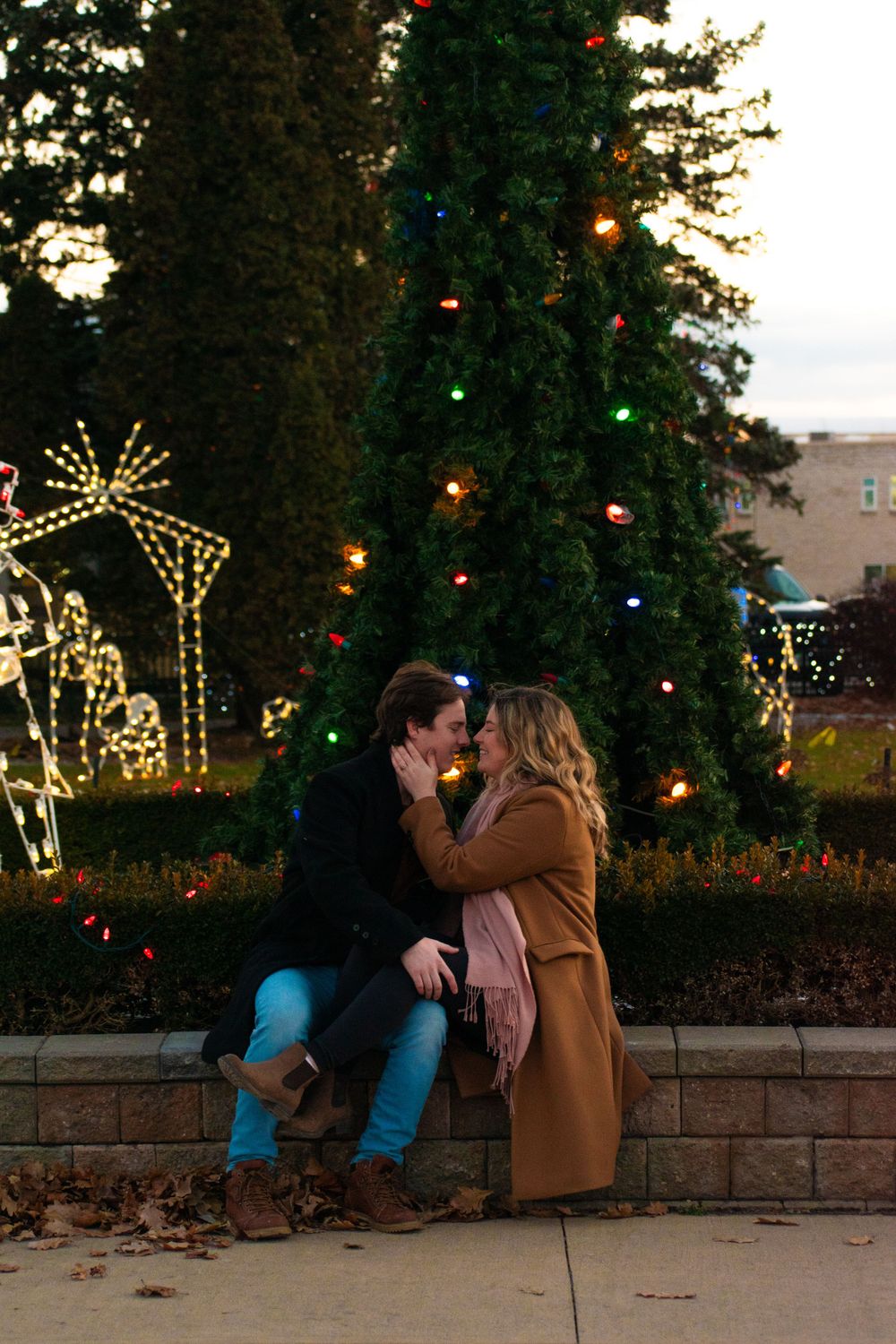 A romantic moment between a couple near a Christmas tree and lighted reindeer decorations.