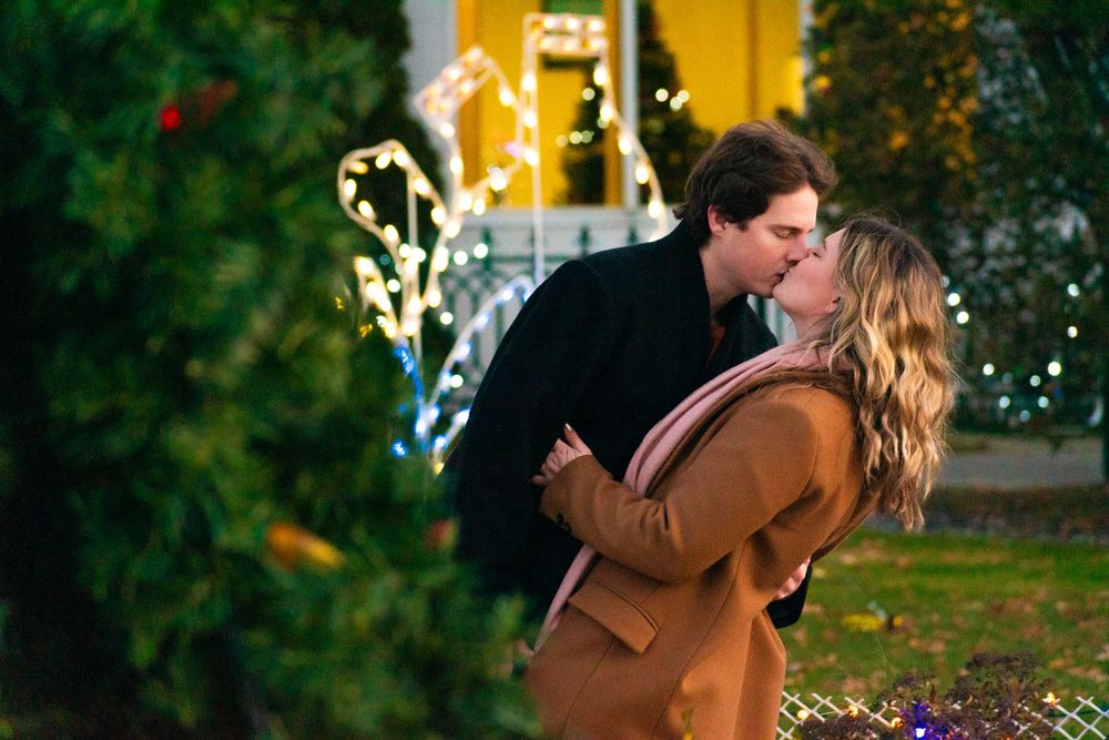 A couple embracing among holiday lights and decorations at dusk.