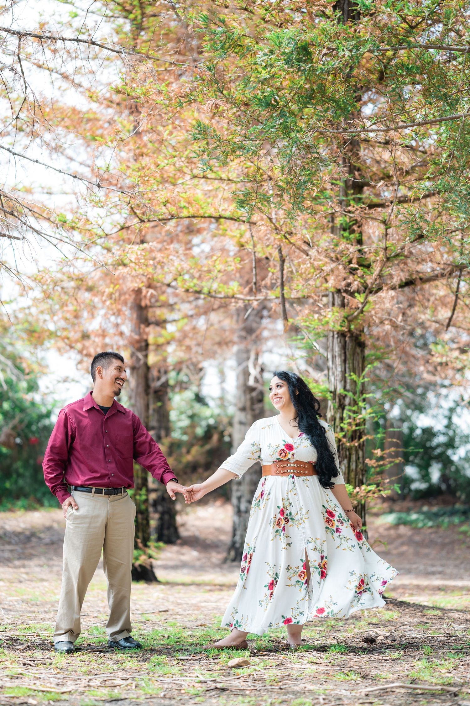 A couple holds hands in a romantic autumn forest setting with fall colors.