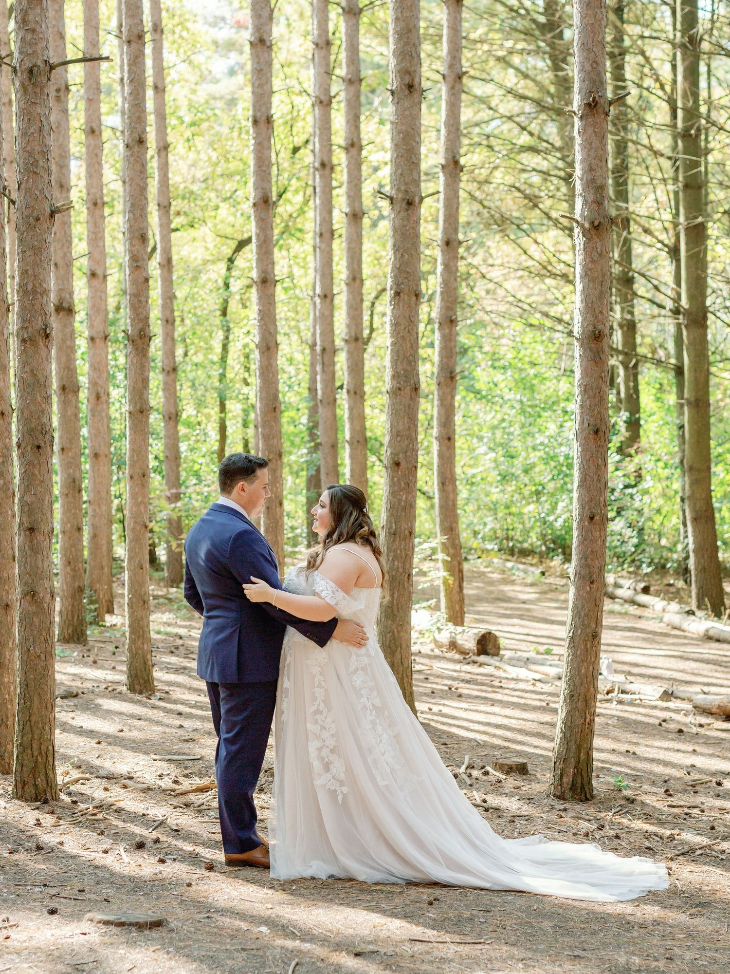 A couple stand holding each other lovingly in a bright forest. Photo by Katie Crane Photography.