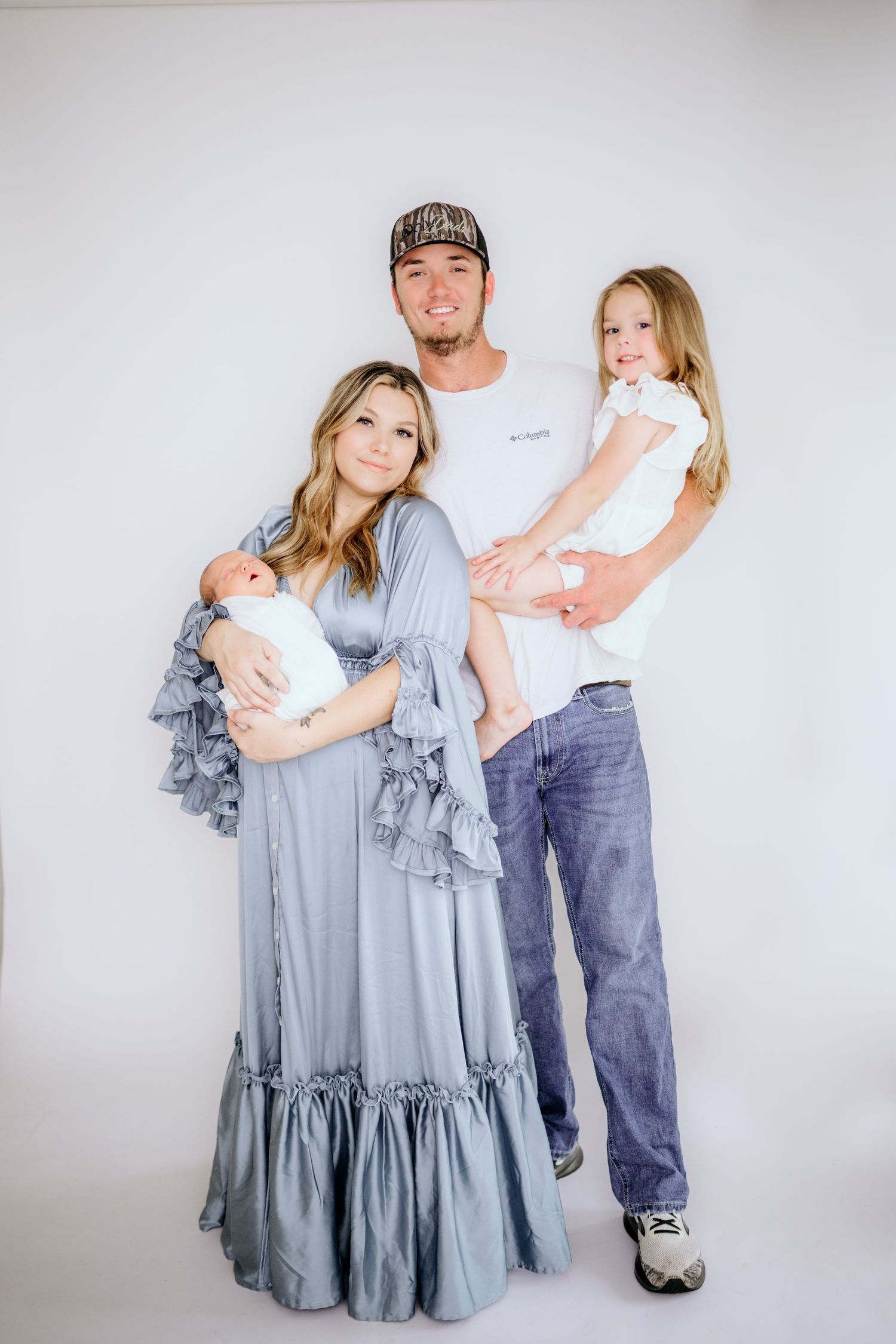 Studio family portrait with parents in coordinating outfits against white background.
