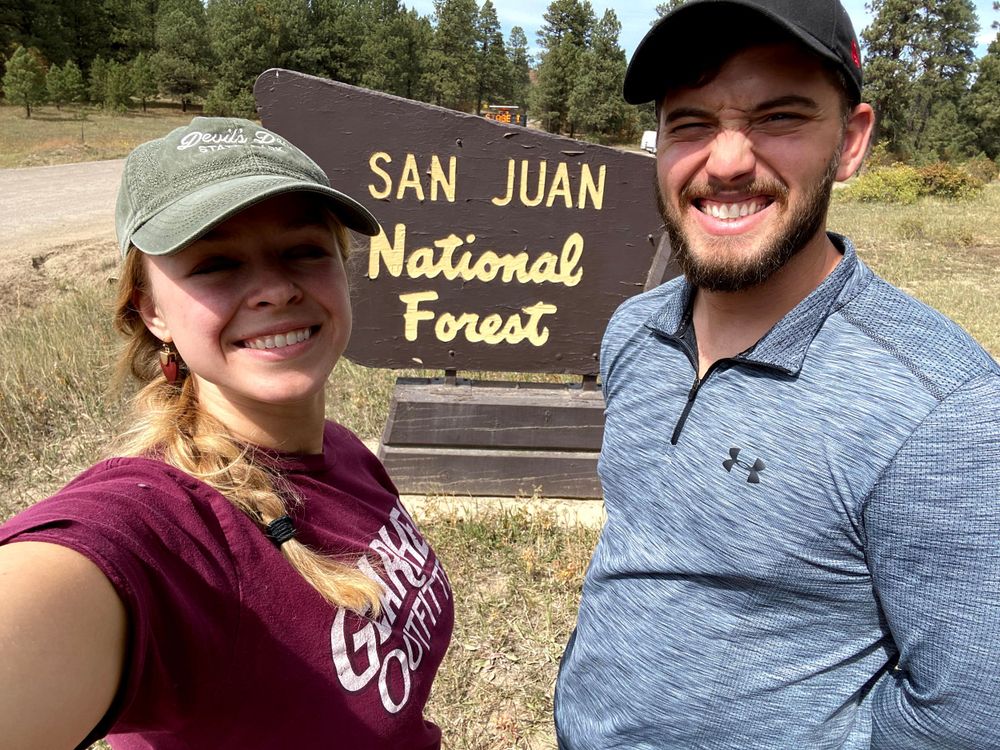 Couple standing in front of San Juan National Forest Sign