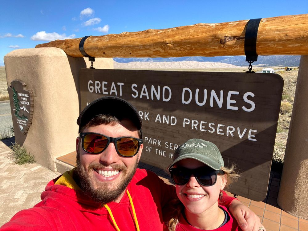Couple standing in front of Great Sand Dunes National Park Sign