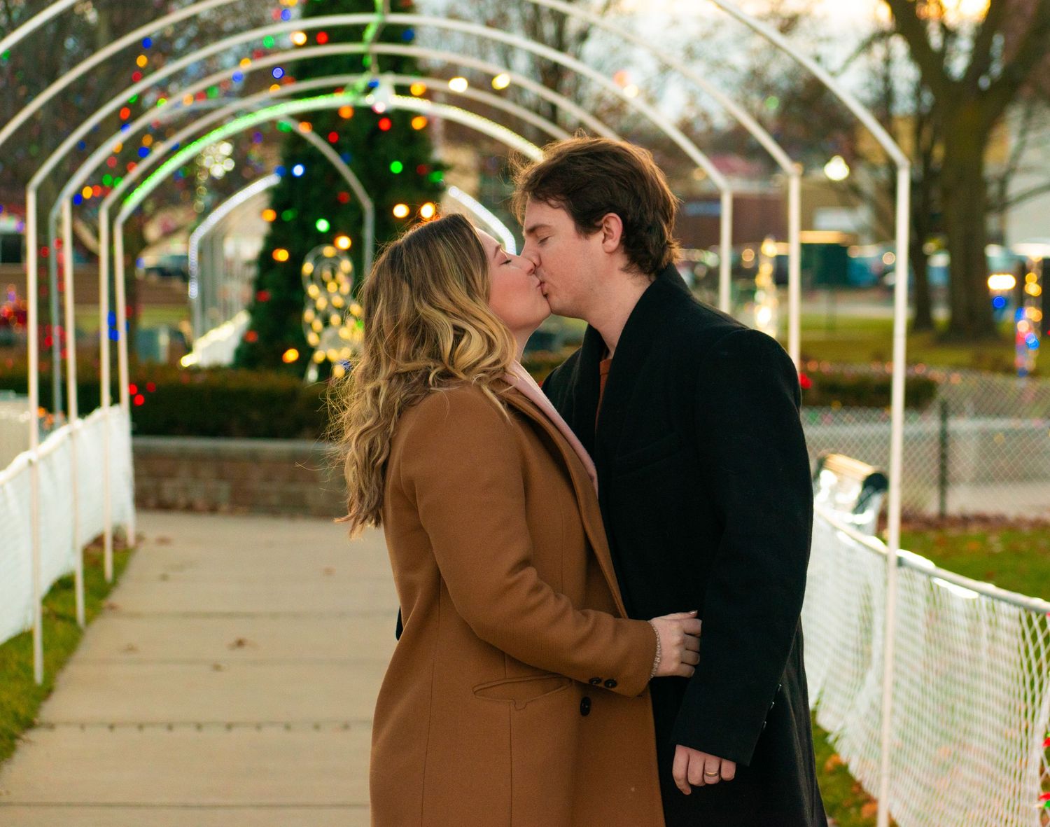 A couple shares a romantic moment under a festive holiday archway.
