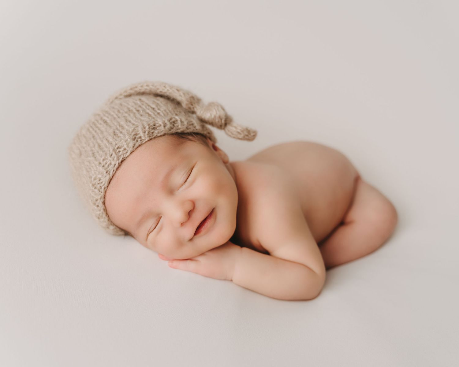 Peaceful sleeping newborn wearing knit bonnet on light backdrop.